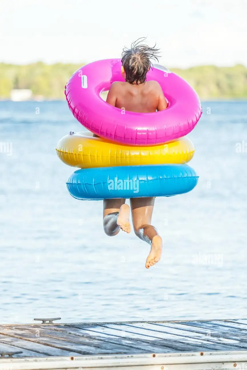 boy-jumping-off-of-dock-by-balsam-lake-wearing-colorful-inflatable-FG6N67~2.webp