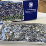 The image shows the completed Everton Mishmash jigsaw puzzle, a highly detailed and colourful illustration depicting the history of Everton Football Club. The puzzle is filled with cartoon-style drawings of famous players, managers, and iconic moments from the club’s past, set against a backdrop of Goodison Park and other significant Everton-related imagery. The artwork includes speech bubbles, banners, and action-packed scenes that bring Everton’s history to life. The jigsaw is fully assembled, showcasing the intricate design and vibrant colours that make it a visually striking piece for Everton fans.